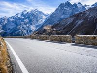 a view of a mountain road going down to a mountain peak with snow capped peaks in the background