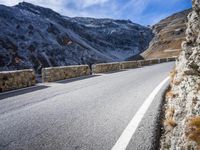 a view of a mountain road going down to a mountain peak with snow capped peaks in the background