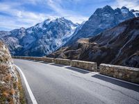 a view of a mountain road going down to a mountain peak with snow capped peaks in the background