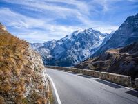 a view of a mountain road going down to a mountain peak with snow capped peaks in the background