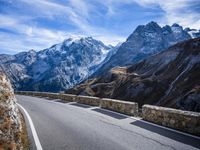 a view of a mountain road going down to a mountain peak with snow capped peaks in the background