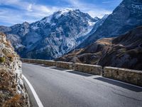 a view of a mountain road going down to a mountain peak with snow capped peaks in the background