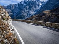 a view of a mountain road going down to a mountain peak with snow capped peaks in the background