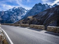 a view of a mountain road going down to a mountain peak with snow capped peaks in the background