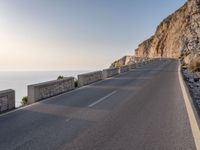 a large long empty road next to a cliff side on the ocean's edge