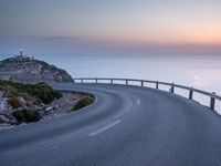 a curved road near the ocean at dusk with a view over the water to the horizon