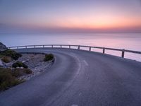 a curved road near the ocean at dusk with a view over the water to the horizon