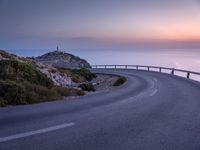 a curved road near the ocean at dusk with a view over the water to the horizon