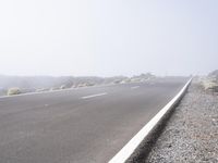 a road near the mountain side in the foggy sun day, and on the opposite bank are hills