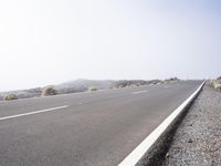 a road near the mountain side in the foggy sun day, and on the opposite bank are hills