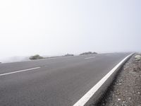 a road near the mountain side in the foggy sun day, and on the opposite bank are hills