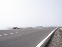 a road near the mountain side in the foggy sun day, and on the opposite bank are hills