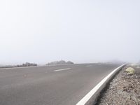 a road near the mountain side in the foggy sun day, and on the opposite bank are hills