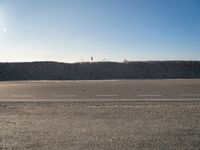 a dirt field that has a hill and sky in the background with rocks and a white line