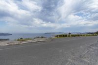 an empty road next to the water and sky with clouds in the background and two motorcycles driving along the road