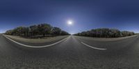 a view of a road through a fisheye lens on an asphalt road with trees and the sun above it