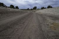 a dirt road through a barren field under cloudy skies with dark clouds in the sky