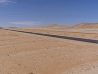 empty road near desert area with mountains in background, no people yet on it, in the distance are bushes and sparse clouds