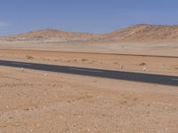 empty road near desert area with mountains in background, no people yet on it, in the distance are bushes and sparse clouds