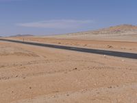 empty road near desert area with mountains in background, no people yet on it, in the distance are bushes and sparse clouds