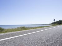 the road stretches out towards a blue body of water on an island on which an upside down sign is leaning on
