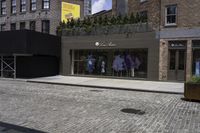 a store in a brick city street with multiple mannequins on the front