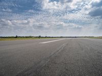 a view of an airplane landing on the runway under clouds in a bright blue sky