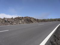 an empty road leading off into a rocky area near the ocean and a hill of rocks