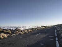 a lone road next to the ocean in the distance, with the mountains and grass on both sides