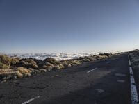 a lone road next to the ocean in the distance, with the mountains and grass on both sides