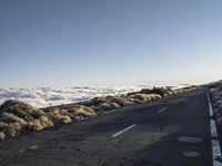 a lone road next to the ocean in the distance, with the mountains and grass on both sides