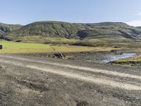 a truck is driving down the mountain road by the field with a stream in it