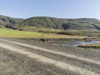 a truck is driving down the mountain road by the field with a stream in it