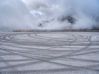 a view from a snowy mountain top with a circular tire on the road surface surrounded by fog and low clouds