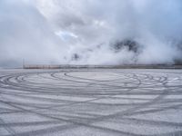 a view from a snowy mountain top with a circular tire on the road surface surrounded by fog and low clouds