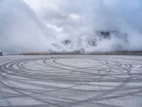 a view from a snowy mountain top with a circular tire on the road surface surrounded by fog and low clouds