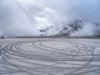 a view from a snowy mountain top with a circular tire on the road surface surrounded by fog and low clouds