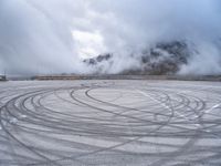 a view from a snowy mountain top with a circular tire on the road surface surrounded by fog and low clouds