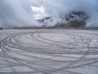 a view from a snowy mountain top with a circular tire on the road surface surrounded by fog and low clouds