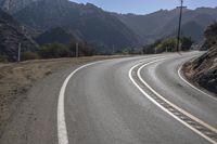 two white lines painted on the road with mountains in the background and a sun shining