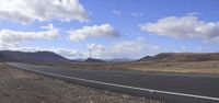 a empty road runs through a desert landscape with hills in the background, on a sunny day