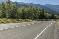 a lone road through a country with mountains in the background on a sunny day with blue sky