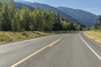 a lone road through a country with mountains in the background on a sunny day with blue sky