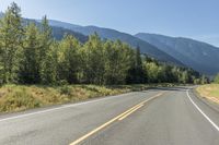 a lone road through a country with mountains in the background on a sunny day with blue sky