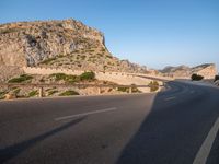 road going through mountain landscape with large rock formation in distance on hilltop side of roadway