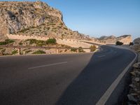 road going through mountain landscape with large rock formation in distance on hilltop side of roadway