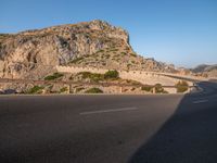 road going through mountain landscape with large rock formation in distance on hilltop side of roadway