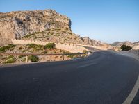 road going through mountain landscape with large rock formation in distance on hilltop side of roadway