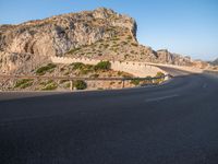 road going through mountain landscape with large rock formation in distance on hilltop side of roadway