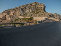 road going through mountain landscape with large rock formation in distance on hilltop side of roadway